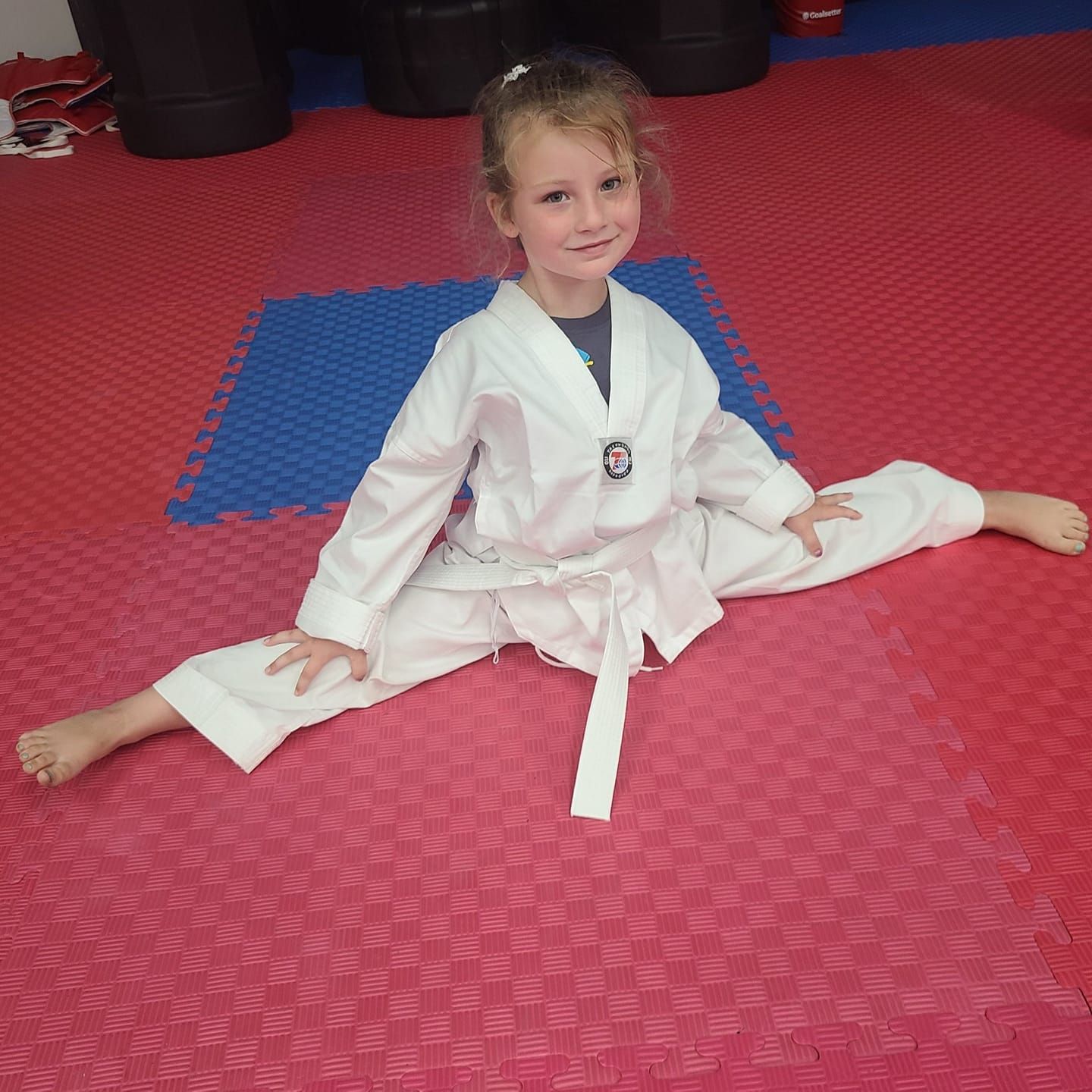 A young girl in a karate uniform is sitting on the floor.