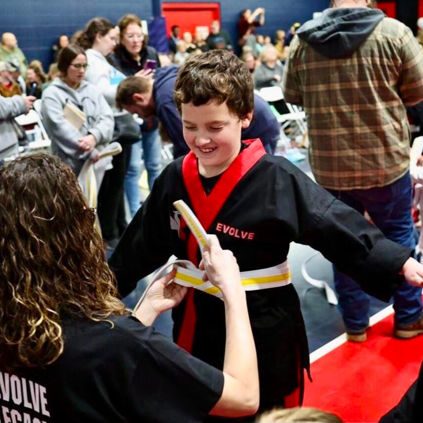 A man is kneeling down next to a young boy in a taekwondo class.