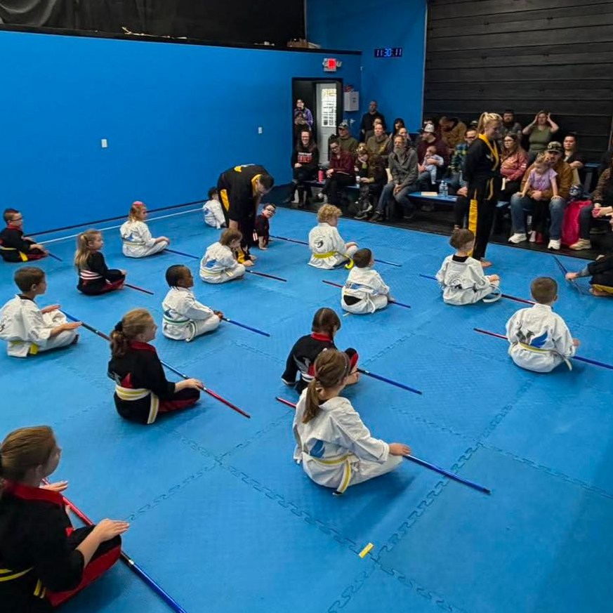 A group of children are practicing karate with a teacher in a gym.
