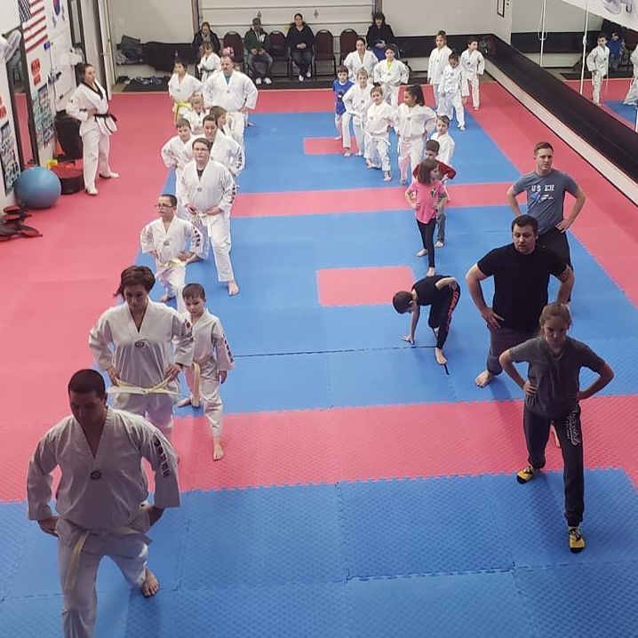 A group of children are practicing karate with a teacher in a gym.