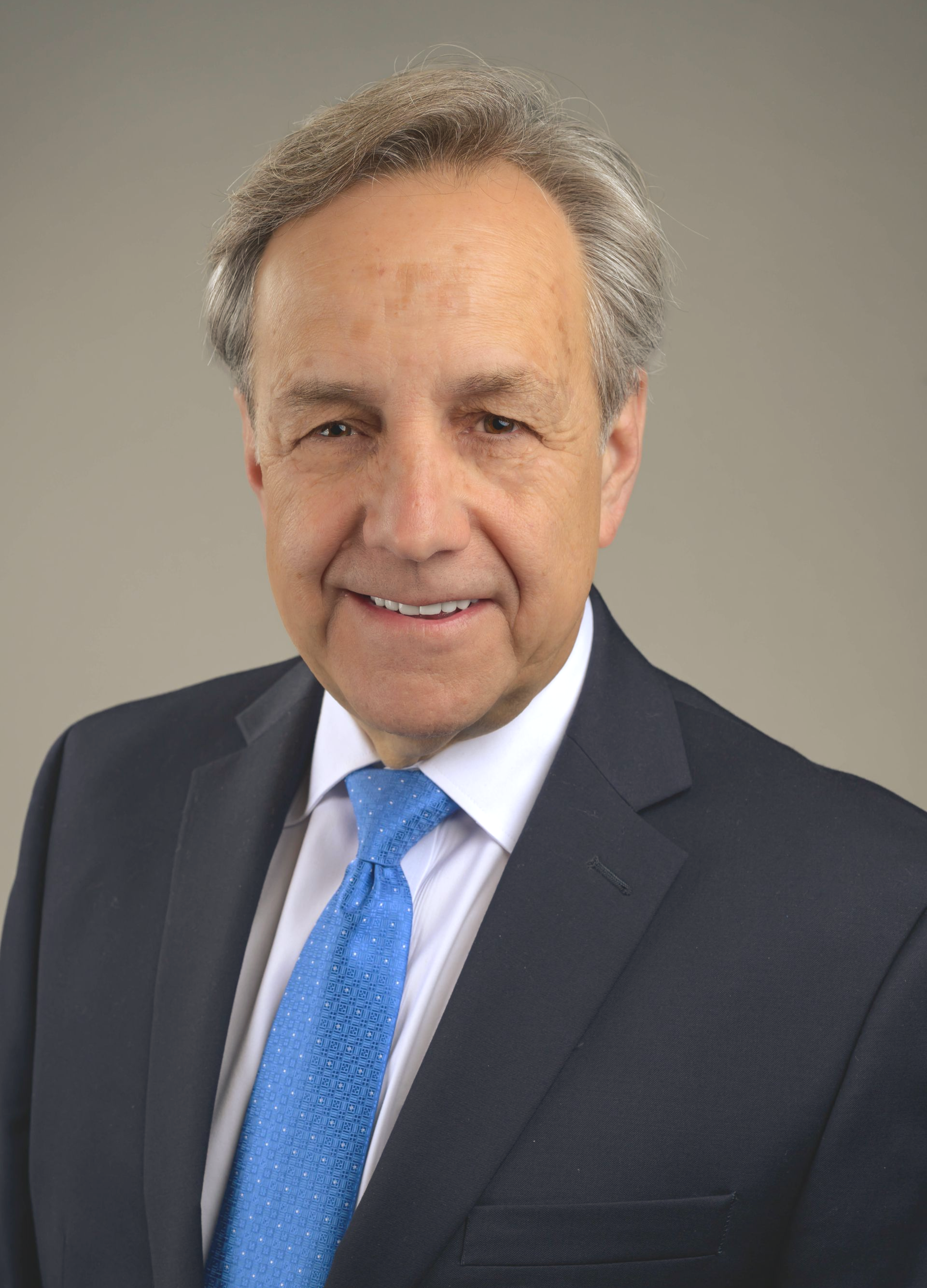 Man in suit and blue tie smiles, head and shoulders portrait.