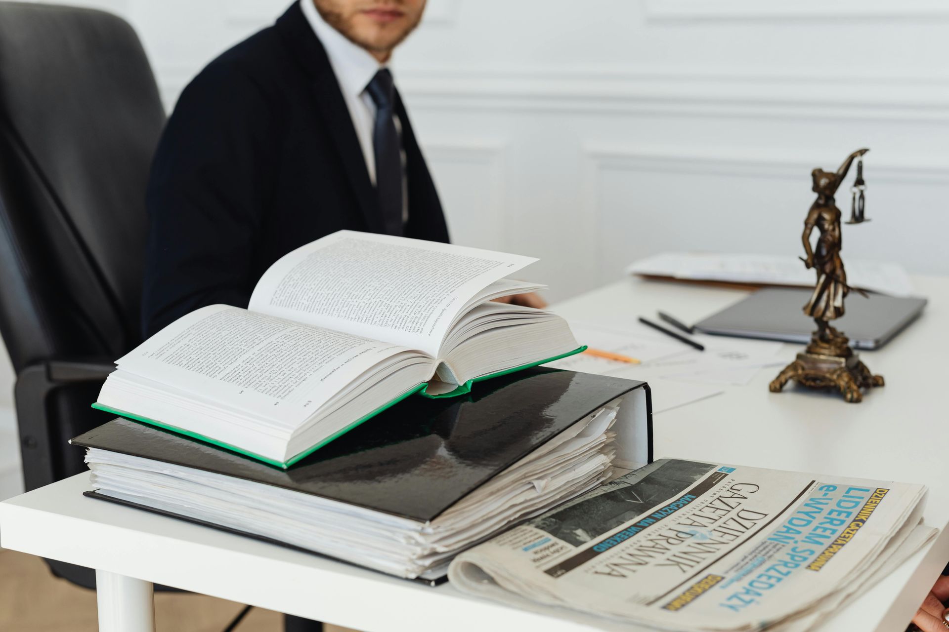 Lawyer at desk with books, files, newspaper, and Lady Justice statue.