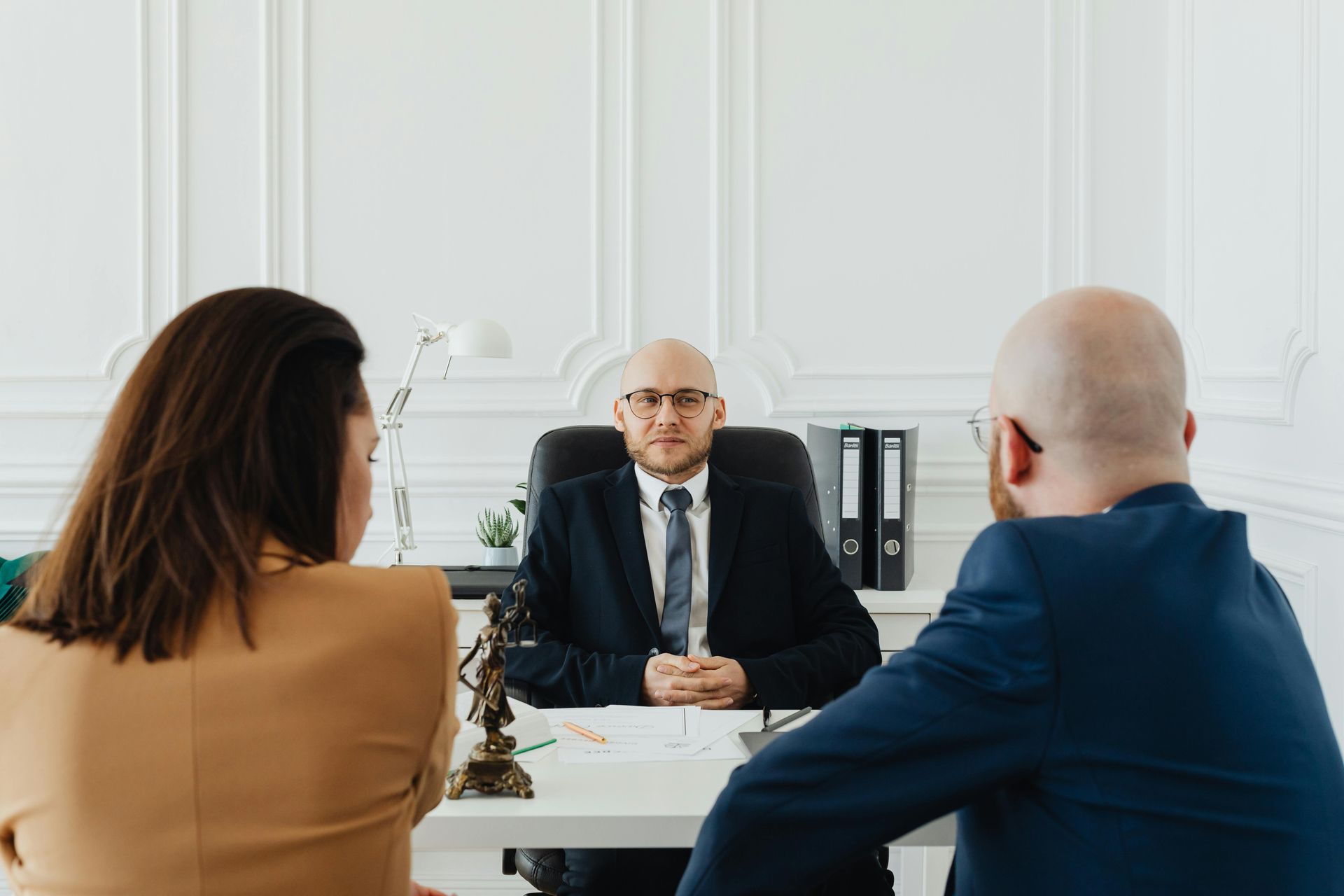 Two people meeting with a bald man in a suit at a bright office desk