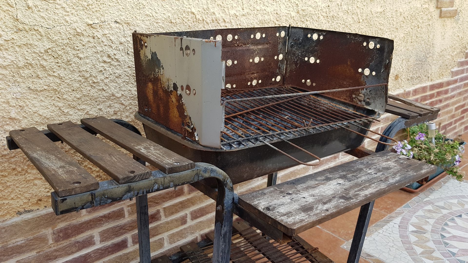 A rusty grill is sitting on a wooden table in front of a brick wall.