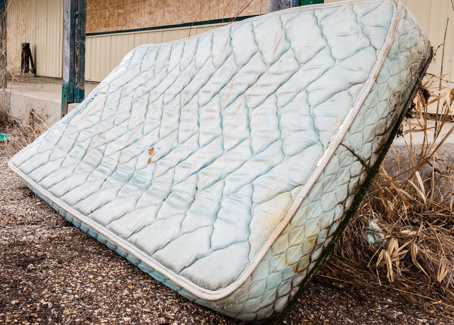 An old mattress is laying on the ground outside of a building.