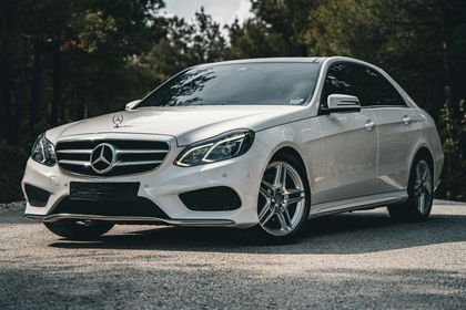 Coupé Mercedes-Benz blanc stationné sur une route, vue de trois quarts avant avec des arbres en arrière-plan