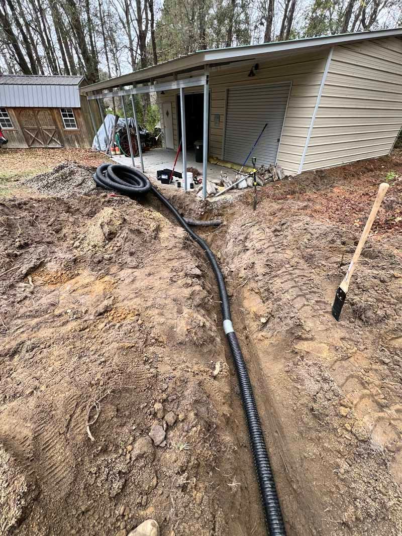Muddy yard with a black hose or pipe leading to a damaged shed with a collapsed wall and scattered debris