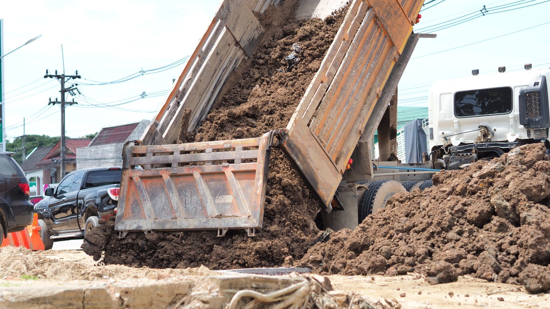 Dump truck unloading soil at a construction site, with a worker nearby and muddy ground.
