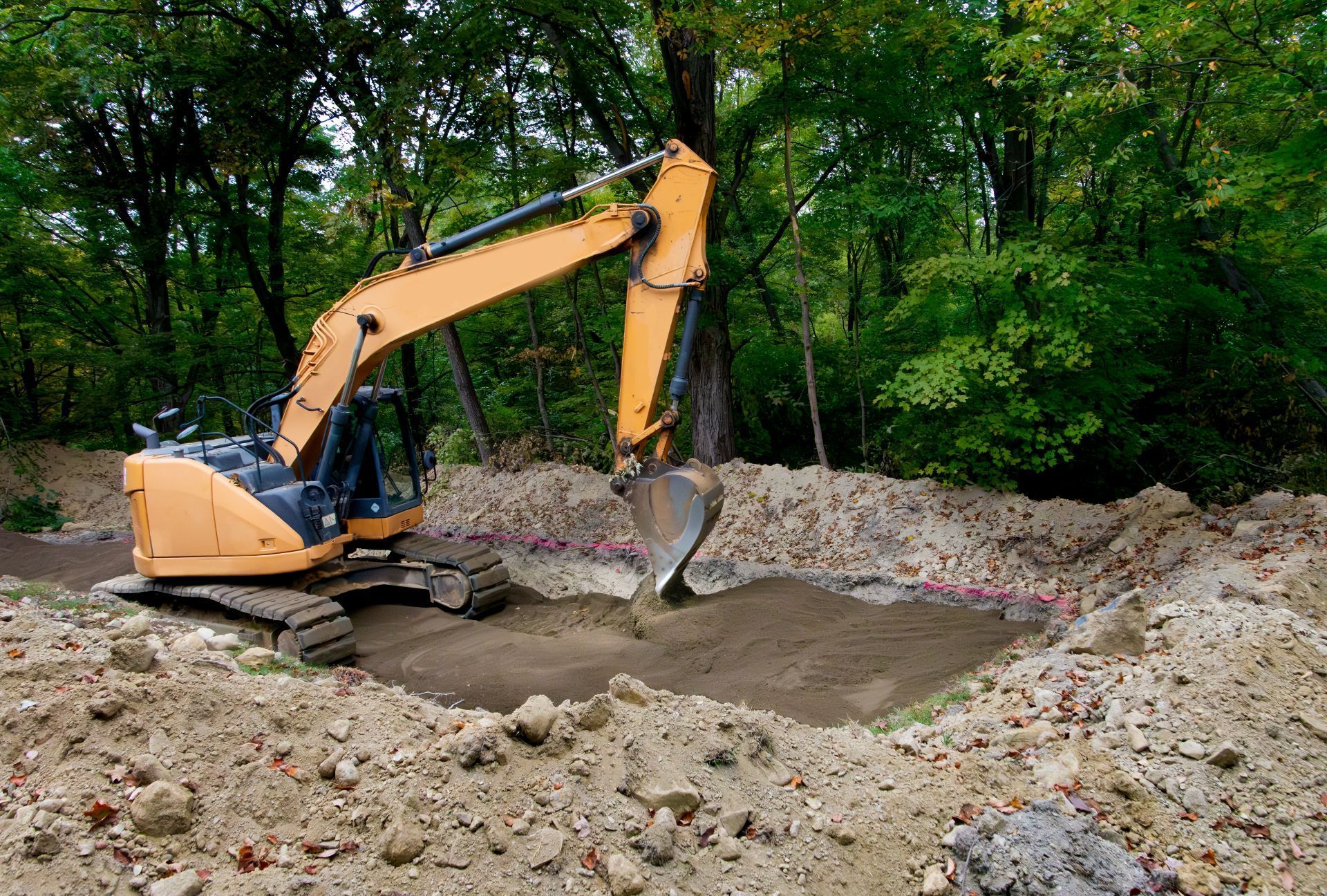 Yellow excavator digging dirt at a construction site beside a wooded area