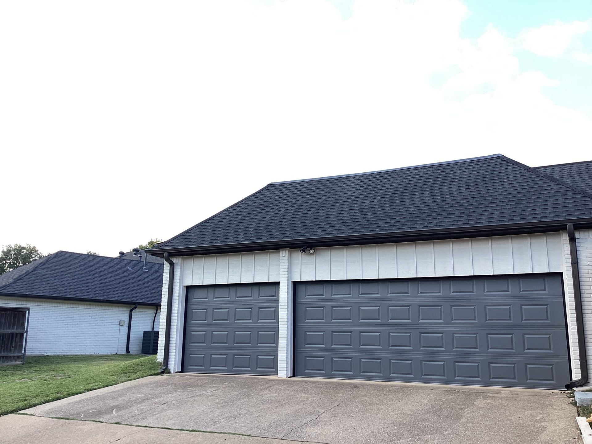 A white house with two garage doors and a black roof.