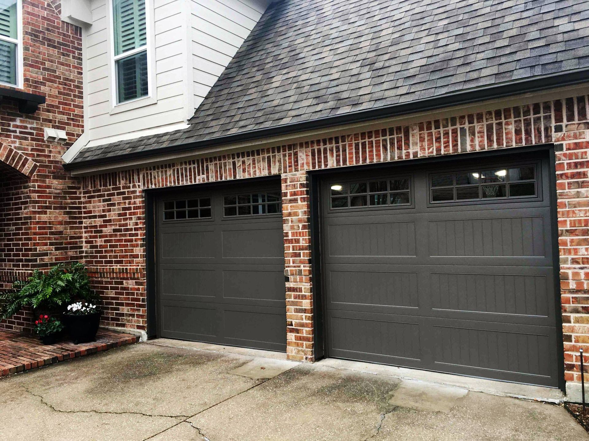 There are two garage doors on the side of a brick house.