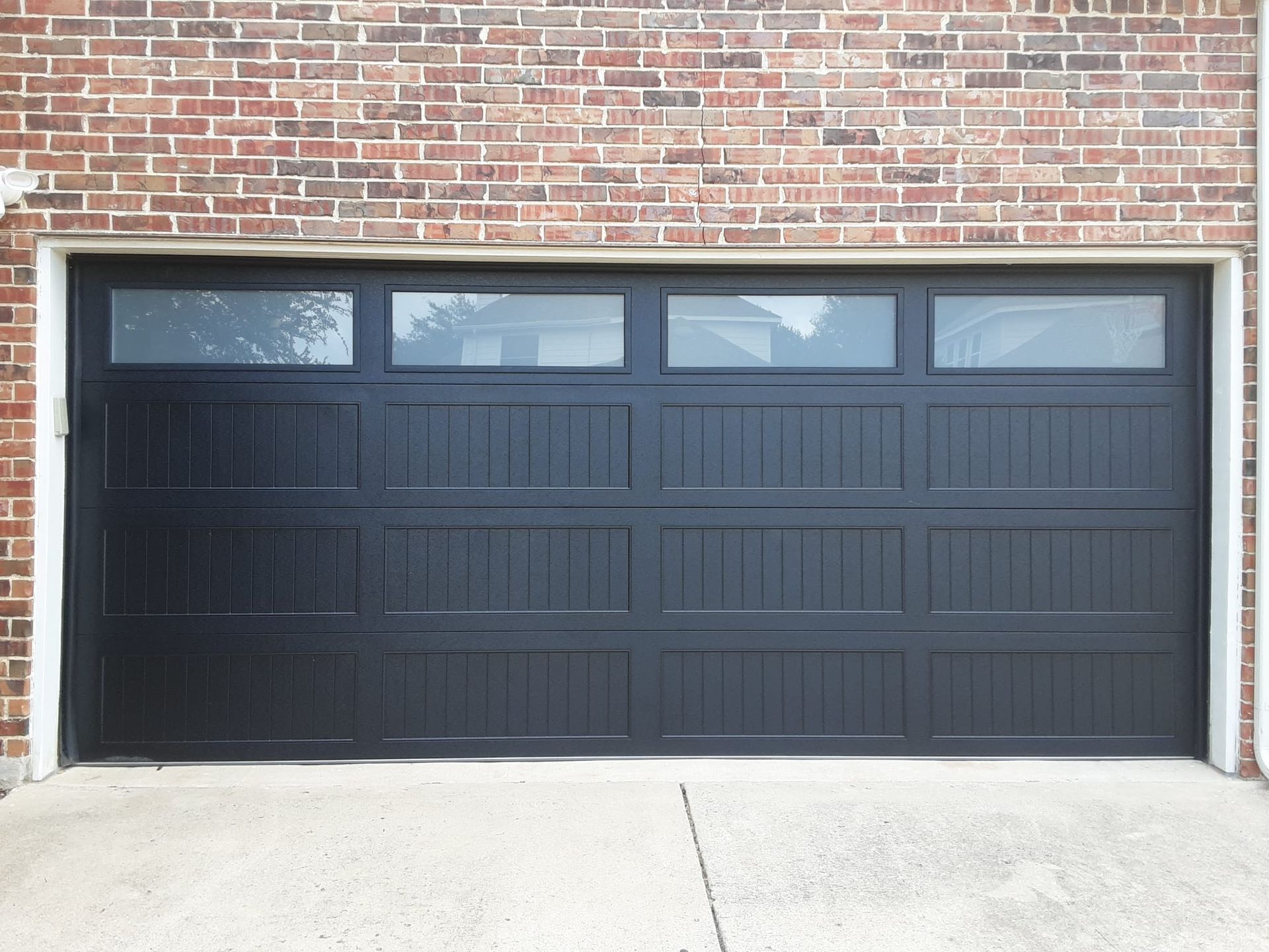 A black garage door is sitting in front of a brick building.