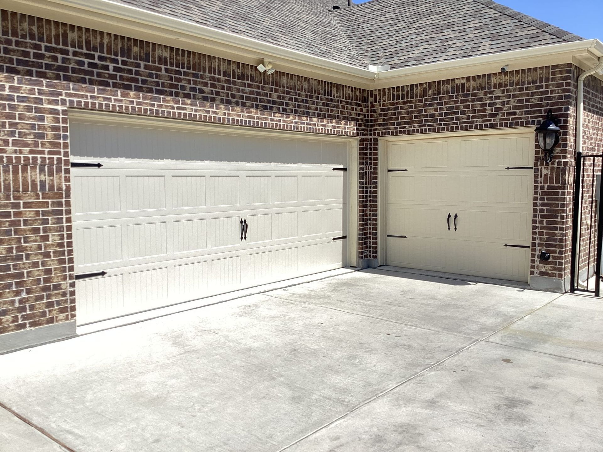 A brick house with two white garage doors and a concrete driveway.