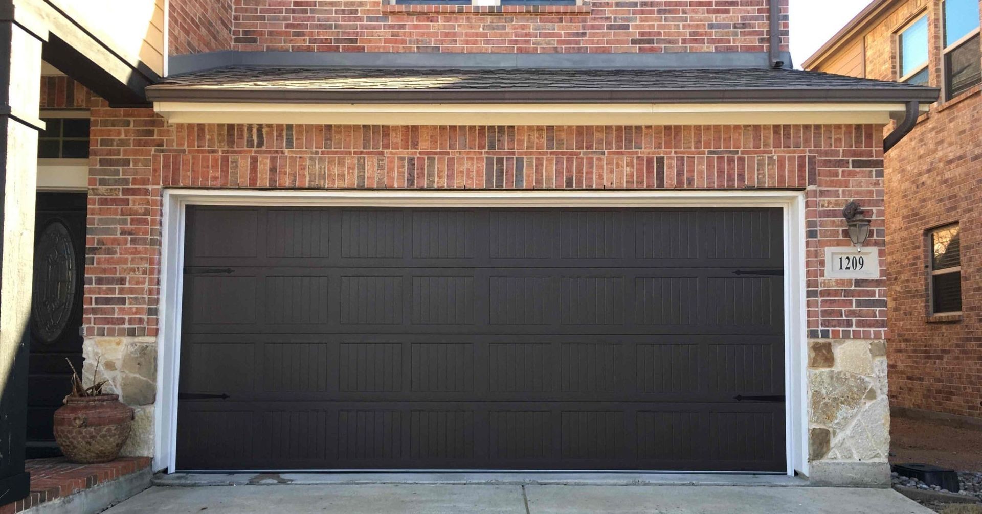 A brown garage door is sitting in front of a brick house.