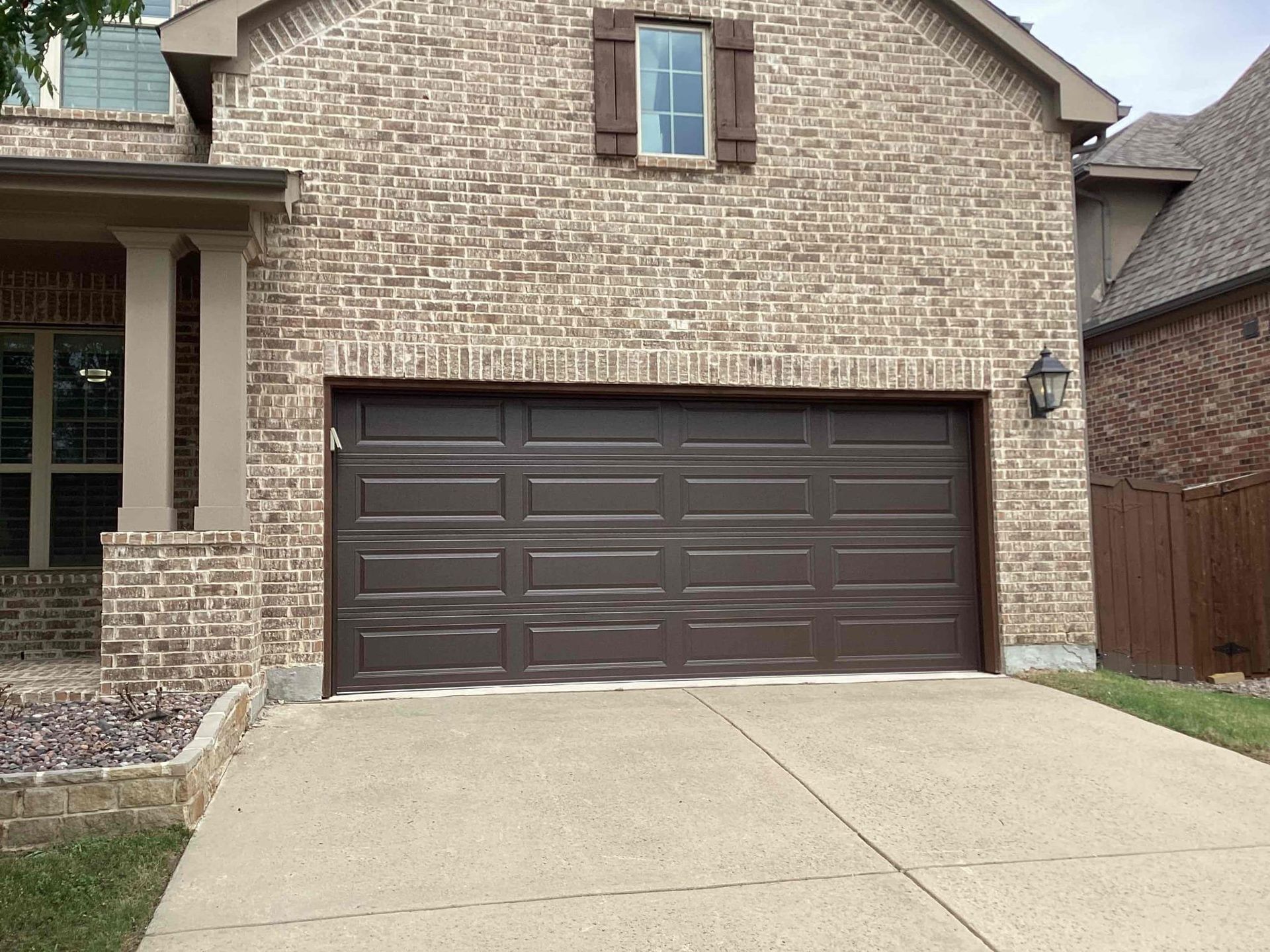 A brown garage door is in front of a brick house.