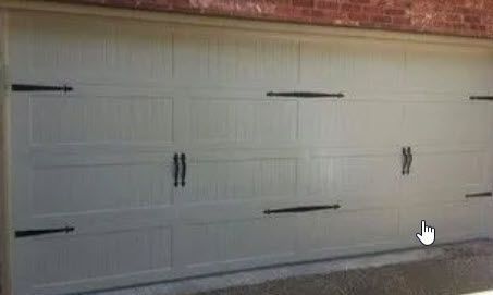 A White Garage Door with Black Handles Is Sitting Next to A Brick Wall.