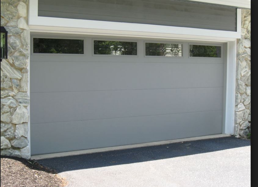 A gray garage door with a stone wall behind it