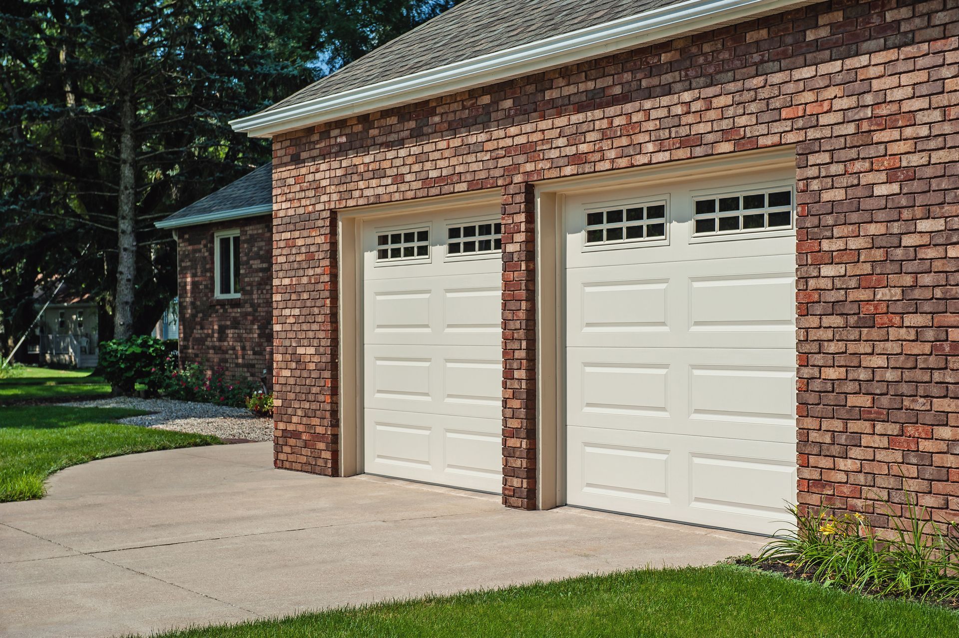 A brick house with two white garage doors and a concrete driveway.