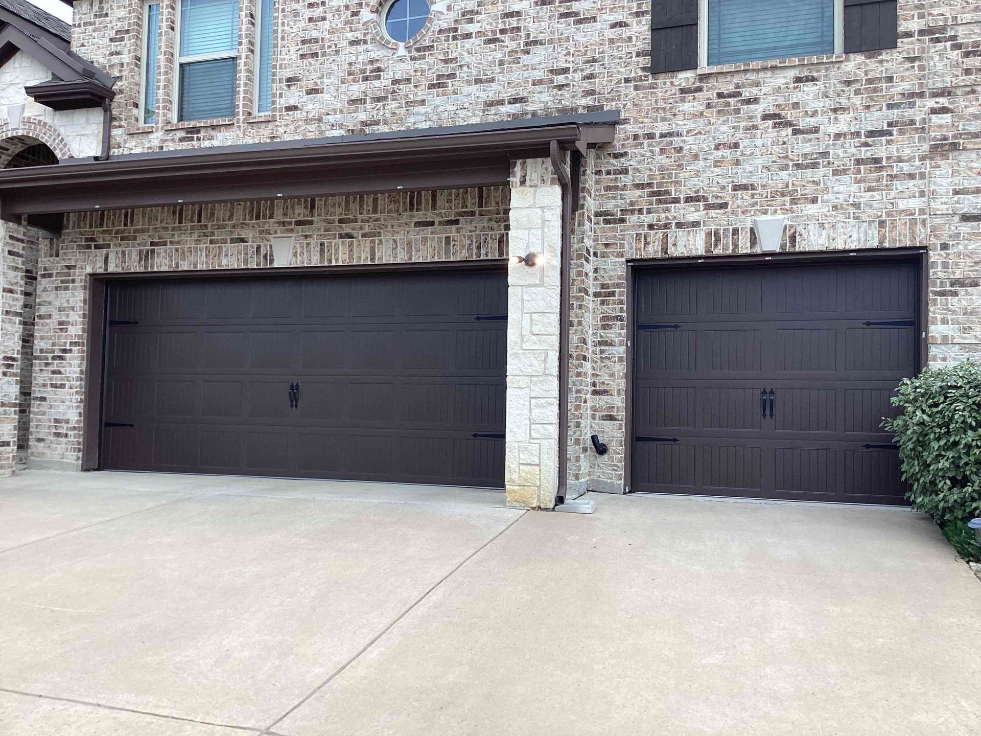 There are two garage doors in front of a brick house.