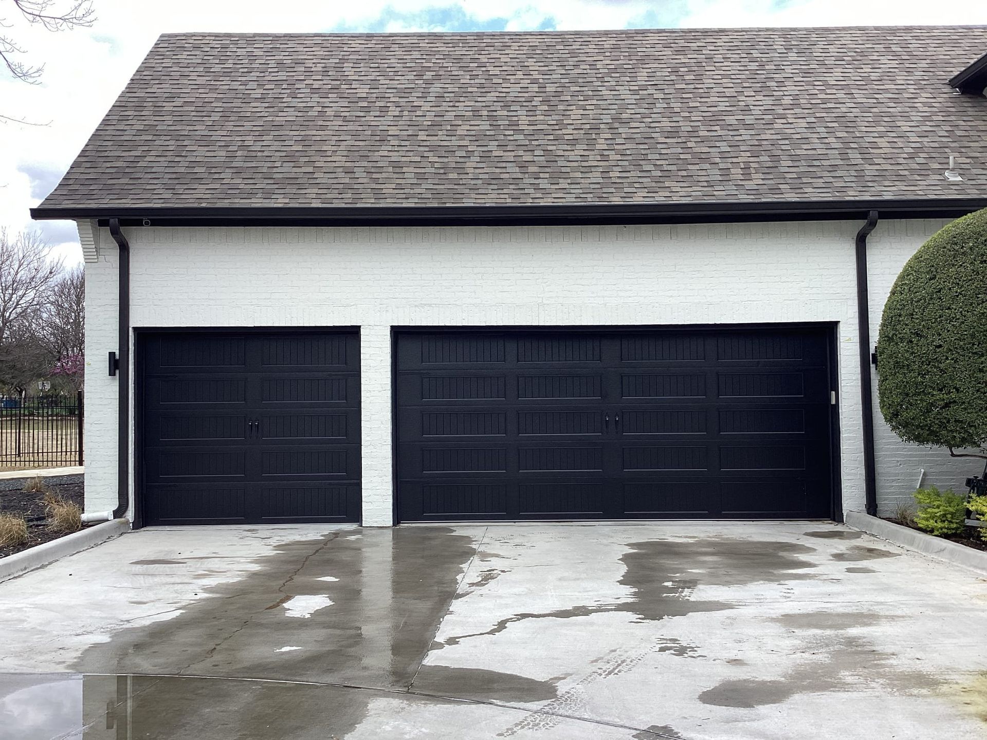 A white house with black garage doors and a concrete driveway.