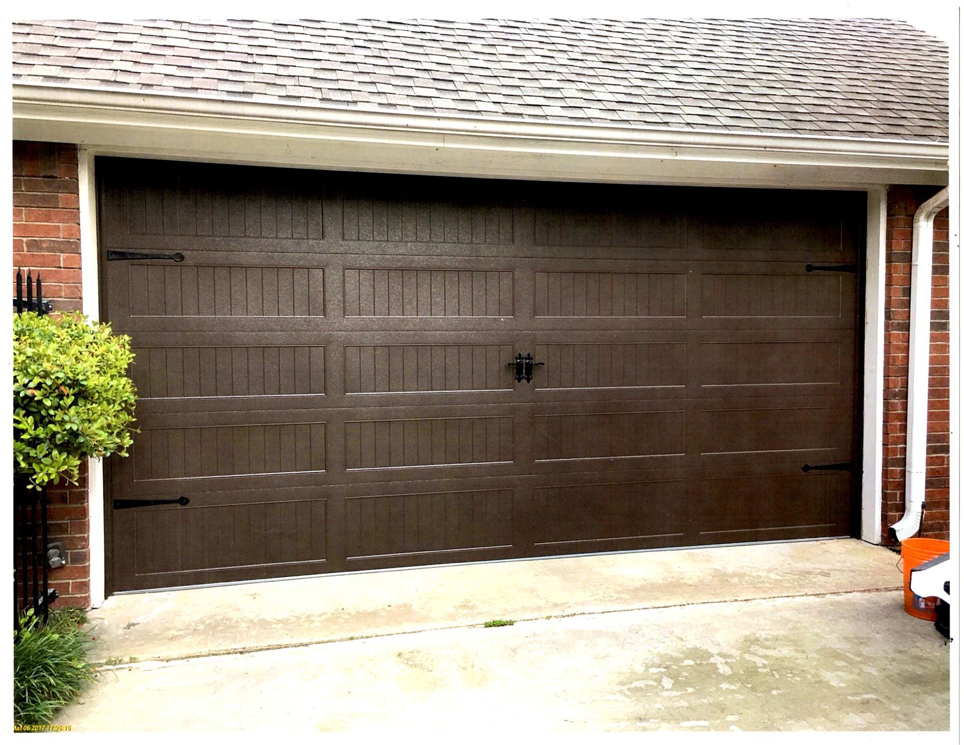 A brown garage door is sitting in front of a brick house.