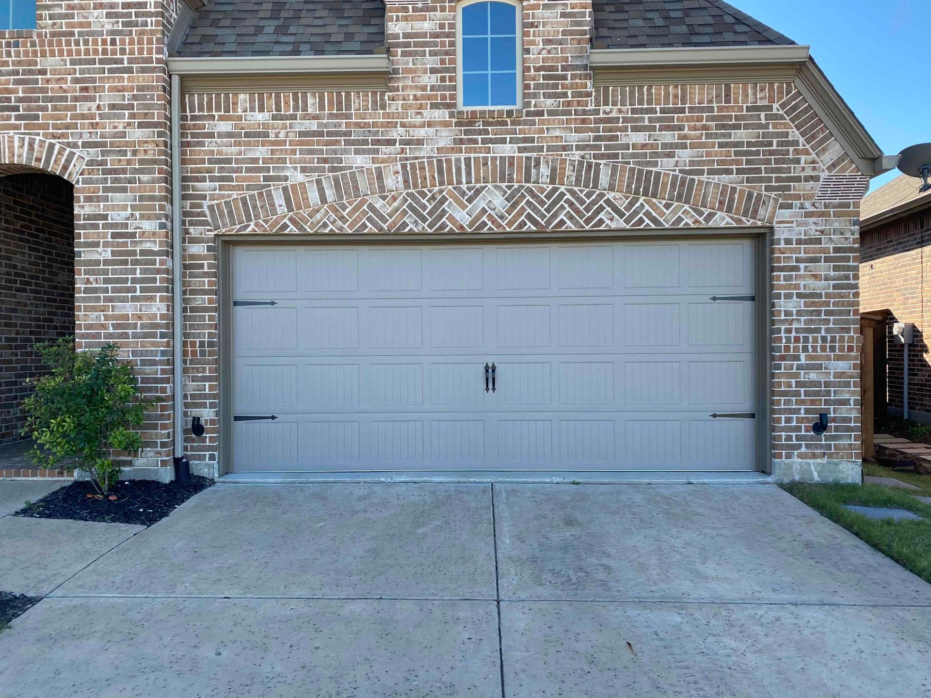 A white garage door is sitting in front of a brick house.