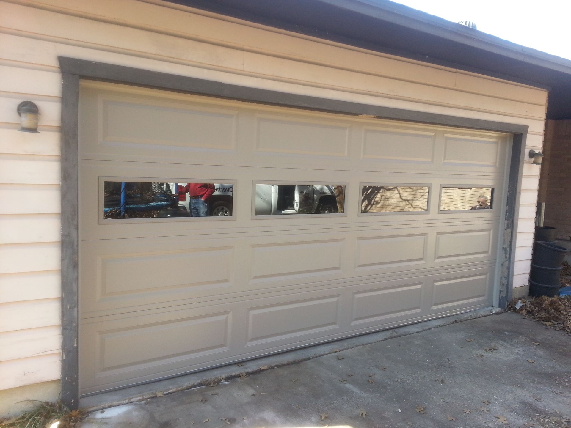 A beige garage door with three windows on the side of a house.
