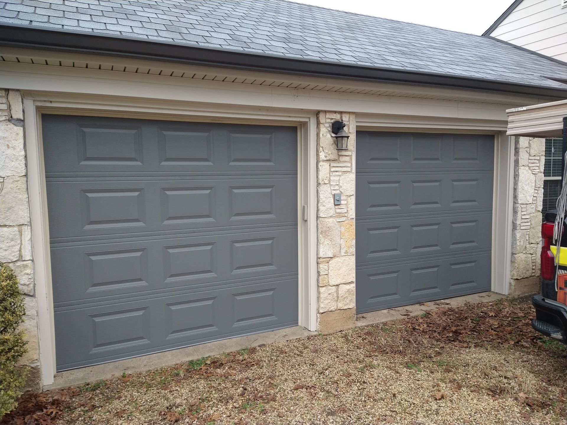 Two gray garage doors are sitting next to each other in front of a house.