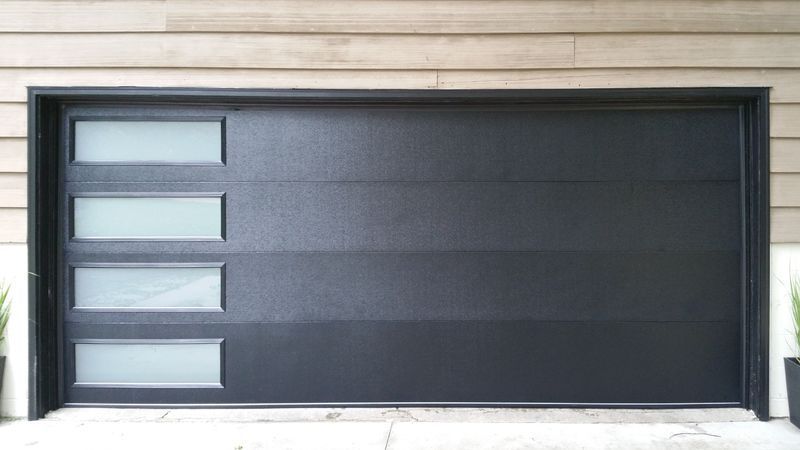 A black garage door with three windows on the side of a house.
