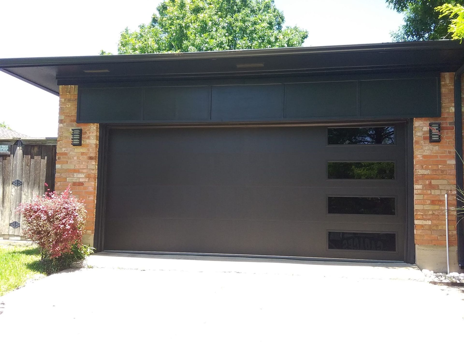 A black garage door is sitting in front of a brick house.