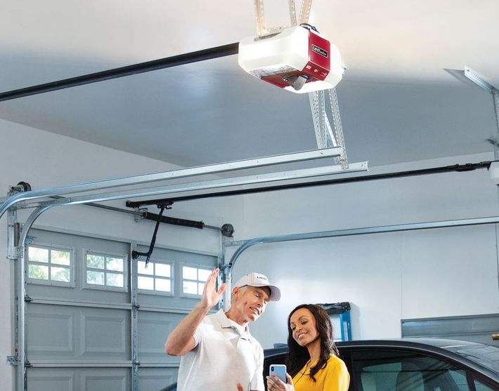 A man and a woman are standing in a garage looking at a garage door opener.