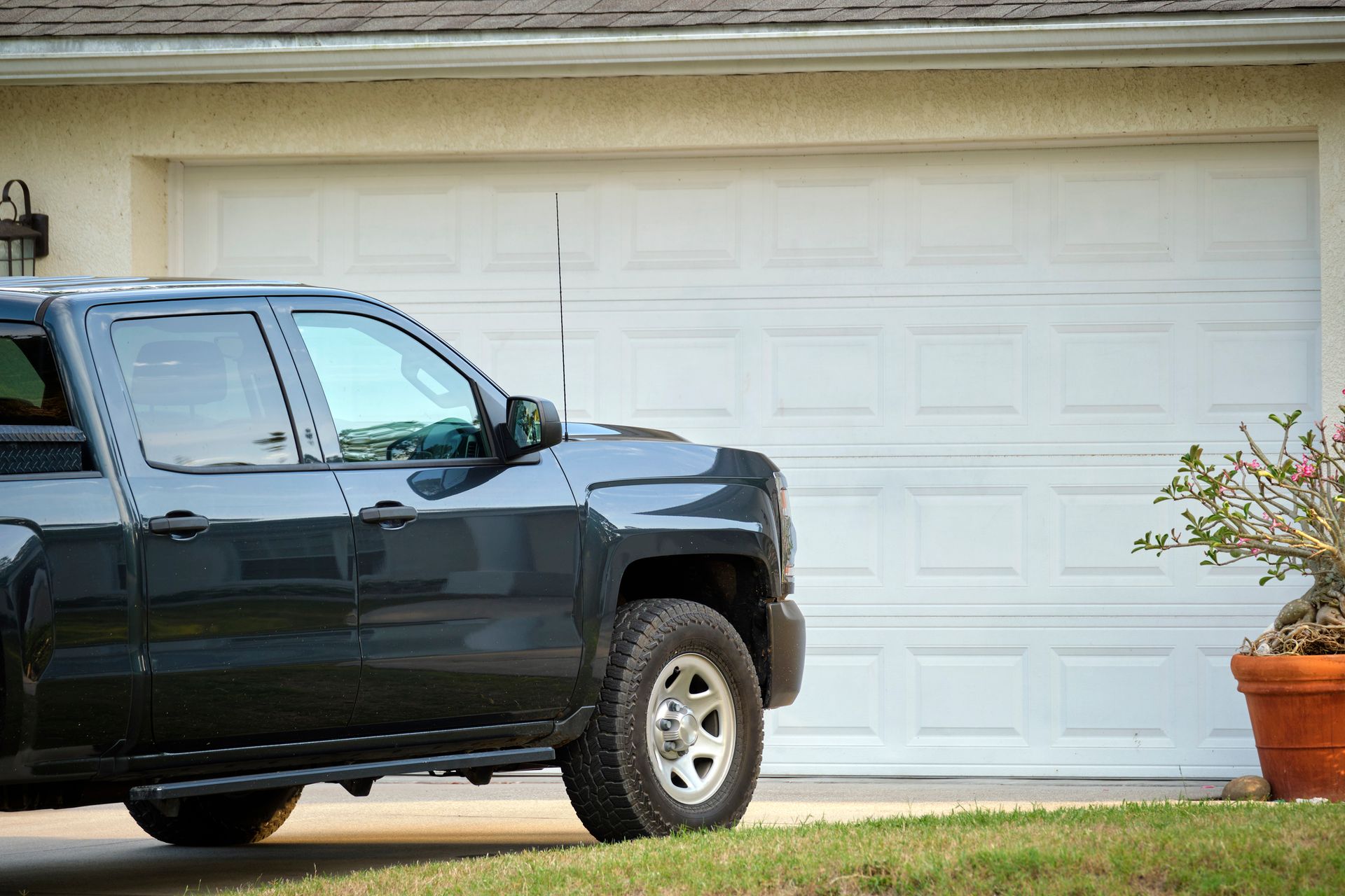 Black car is parked in front of a wide PVC garage door that is closed.