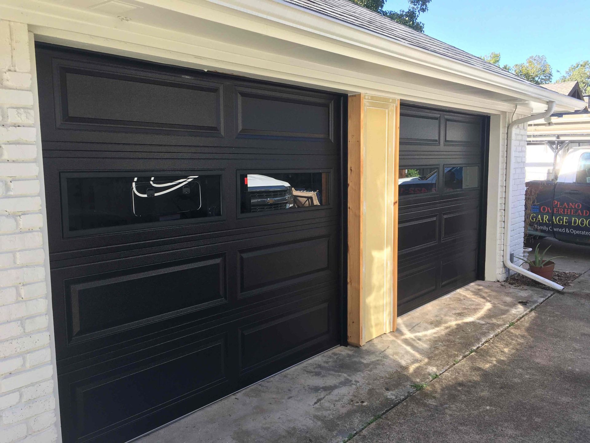 A black garage door is sitting next to a white brick building.