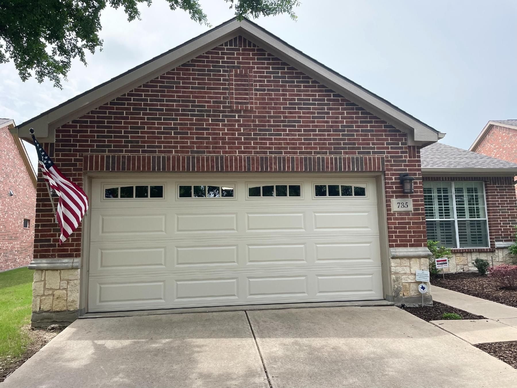 A brick house with a white garage door and an american flag in front of it.