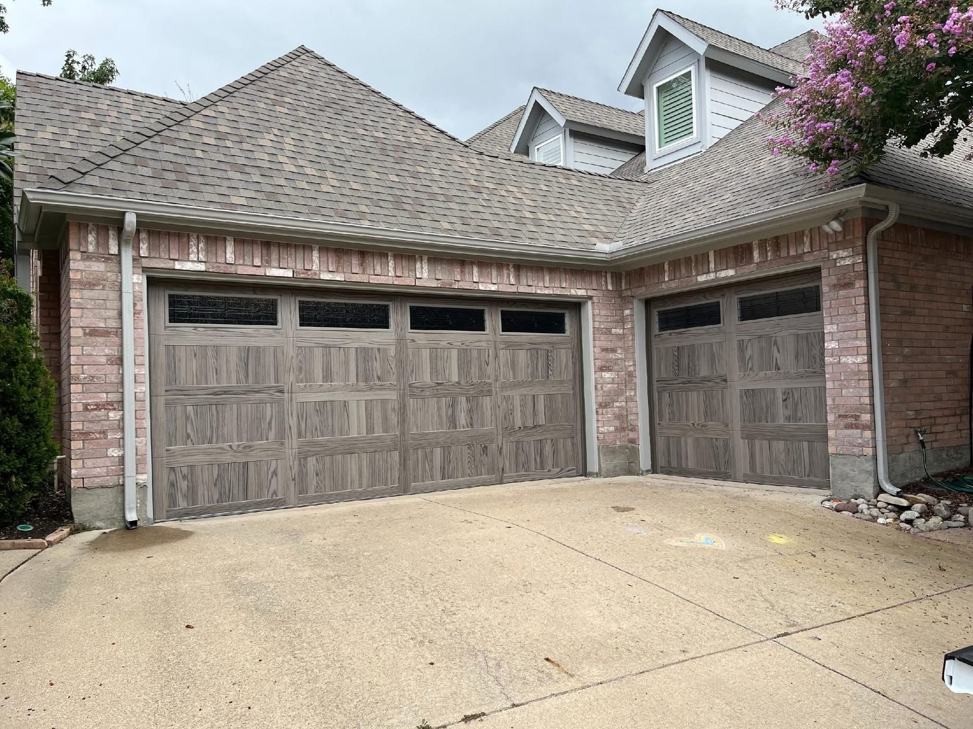 Two-car garage with weathered wood-look doors, brick facade, and a concrete driveway.