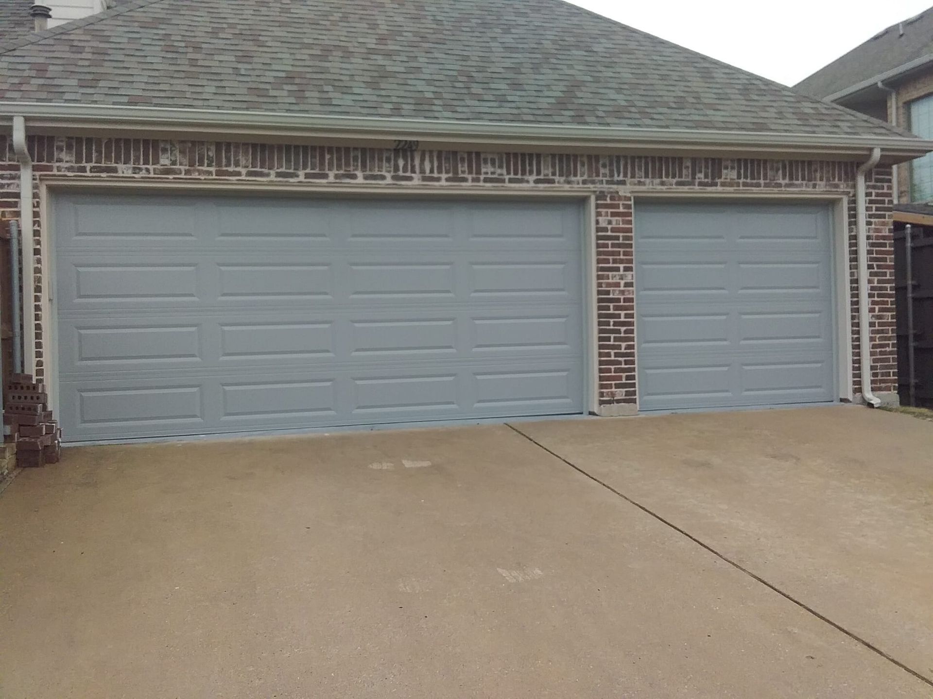 There are two garage doors on the side of a brick house.