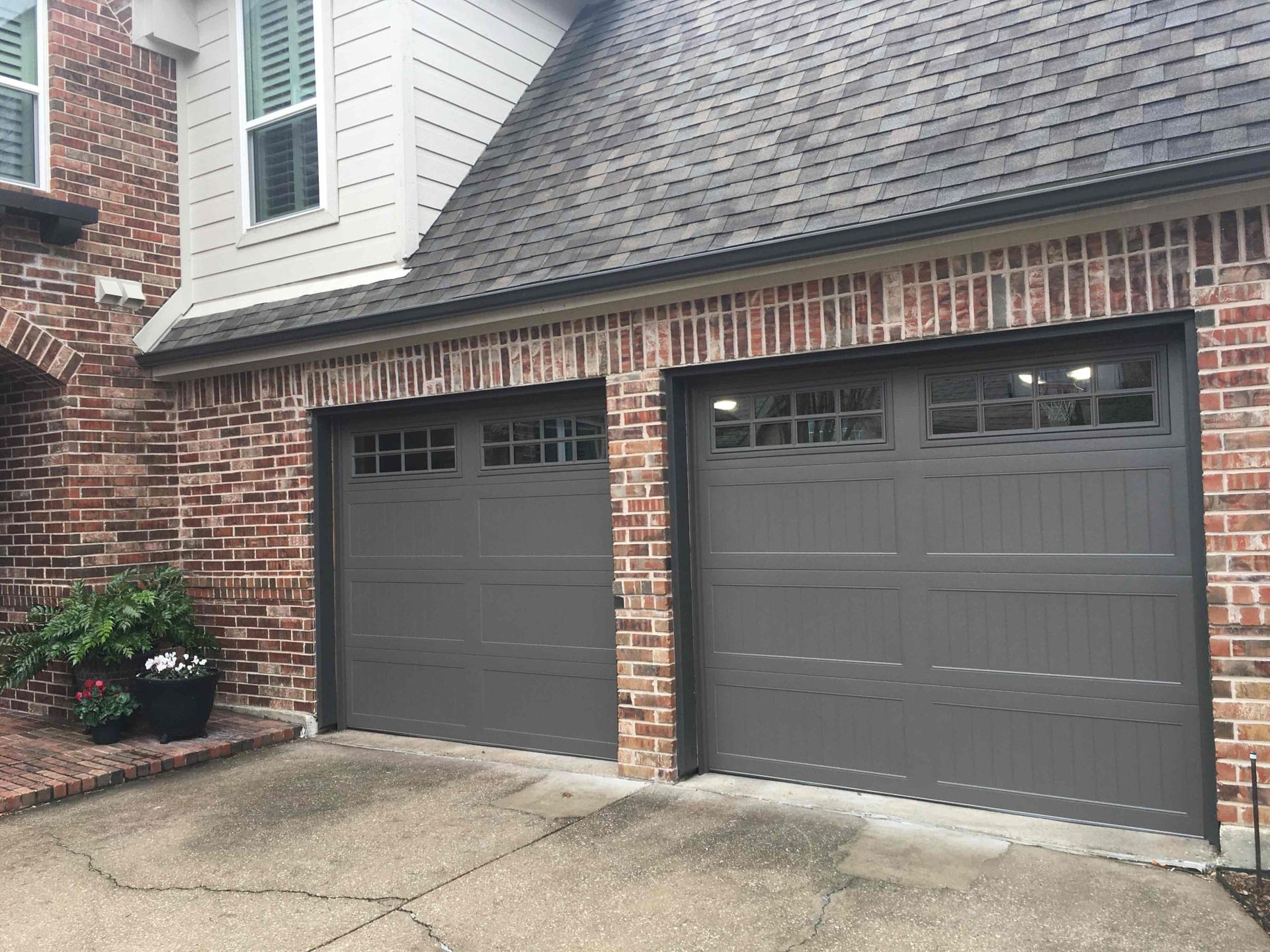 There are two garage doors on the side of a brick house.