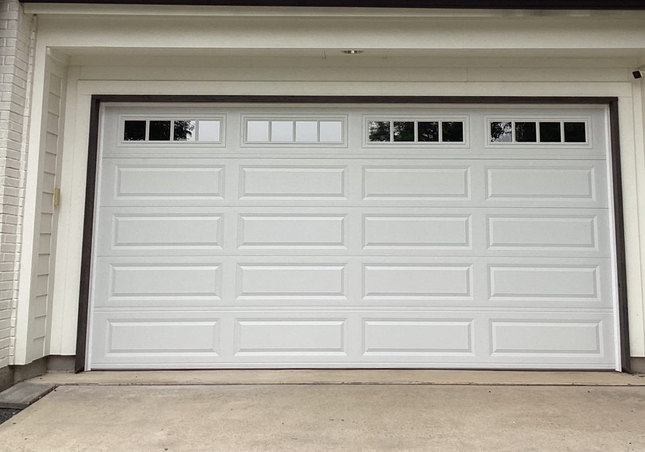 White garage door with windows, concrete driveway, and green bushes.