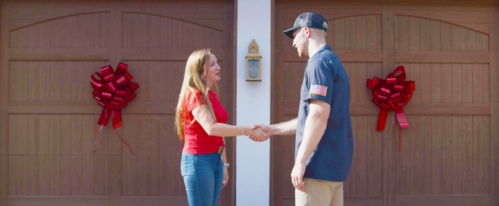 A man and a woman are shaking hands in front of a garage door.