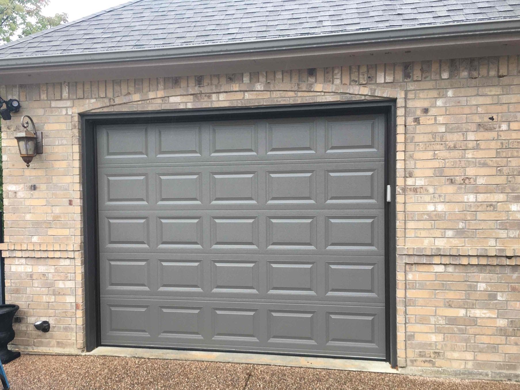 A gray garage door is on a brick building.