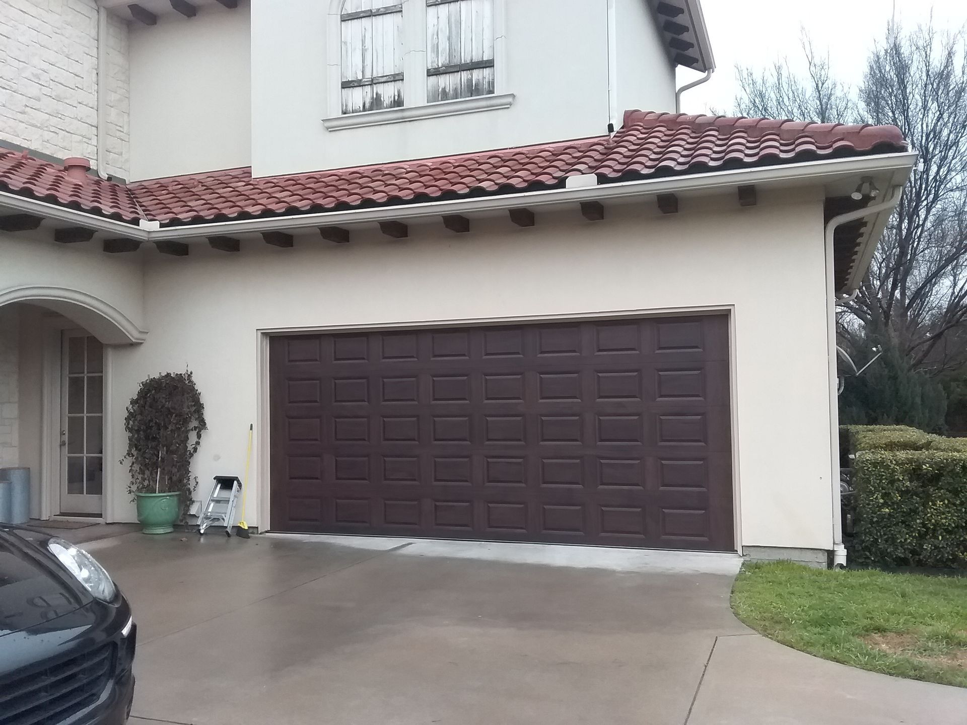 A car is parked in front of a white house with a brown garage door