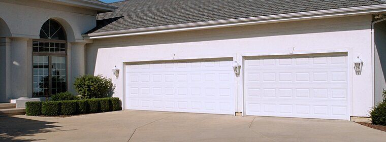 A white house with two white garage doors and a driveway.