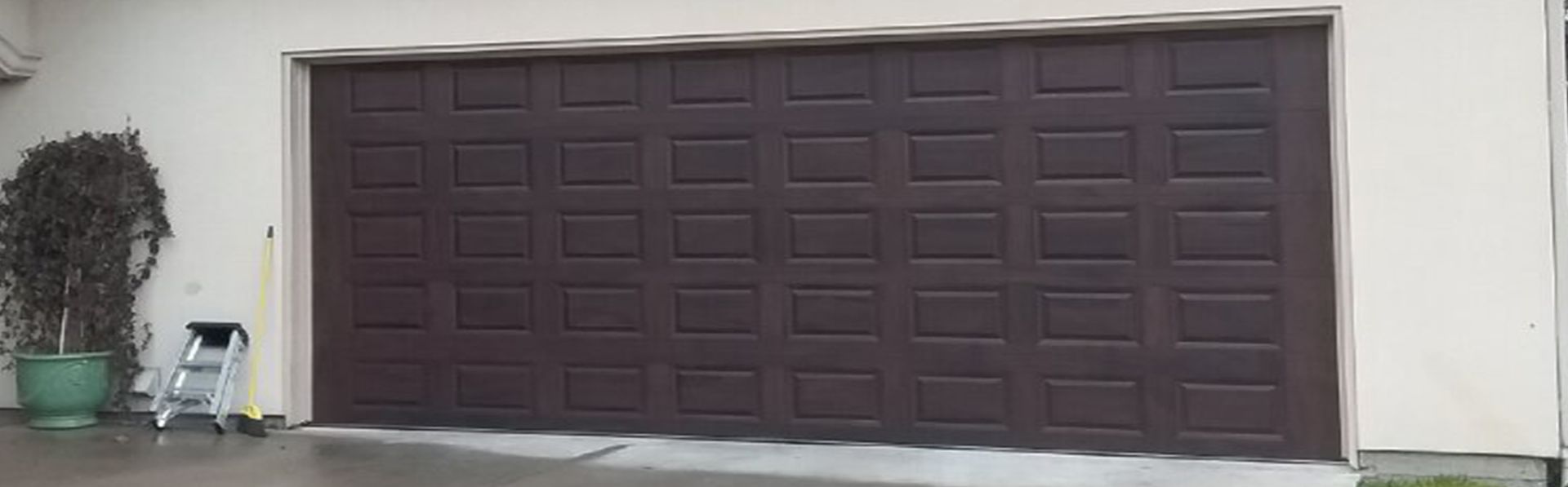 A brown garage door is being painted in front of a house.