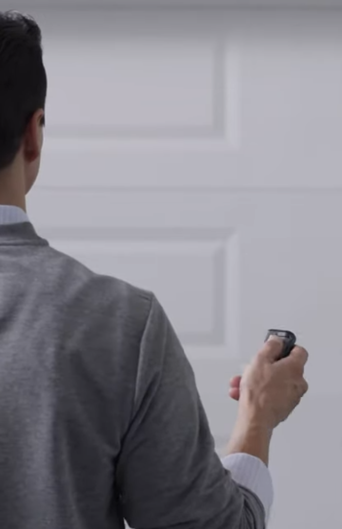 A man, holding a remote control in front of a garage door.