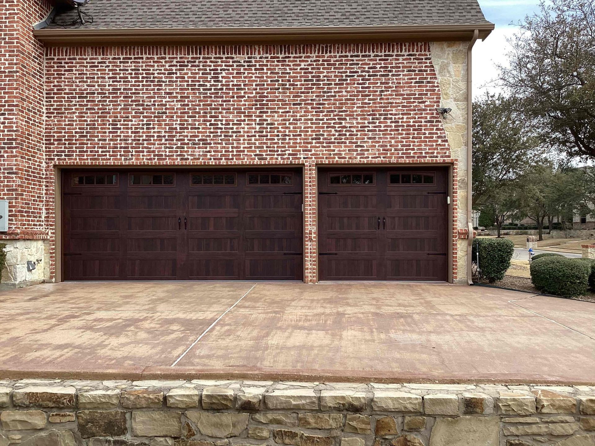 A brick house with two garage doors and a stone wall.