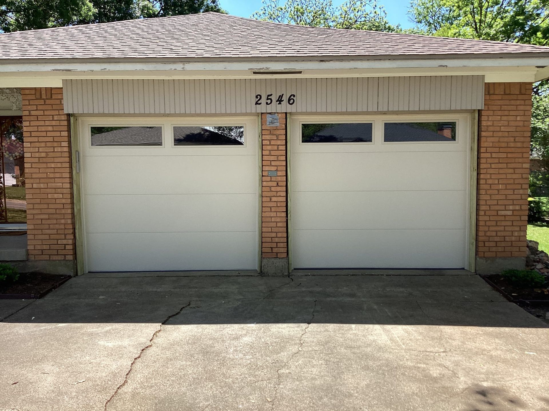 A white garage door is sitting in front of a brick house.