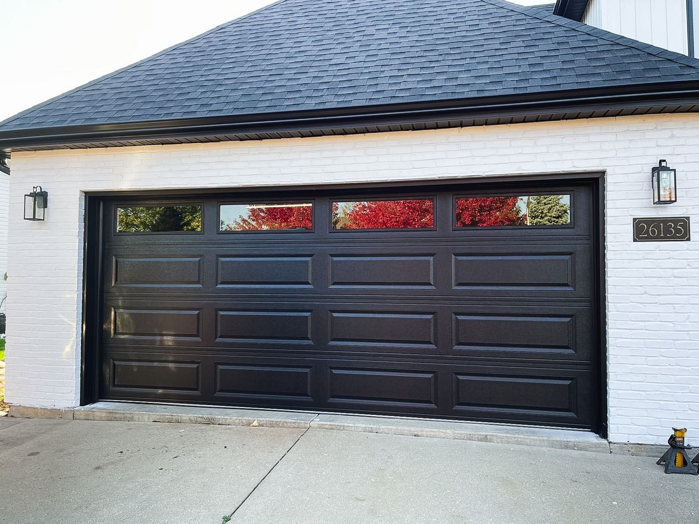 A white brick house with a black garage door and a black roof.