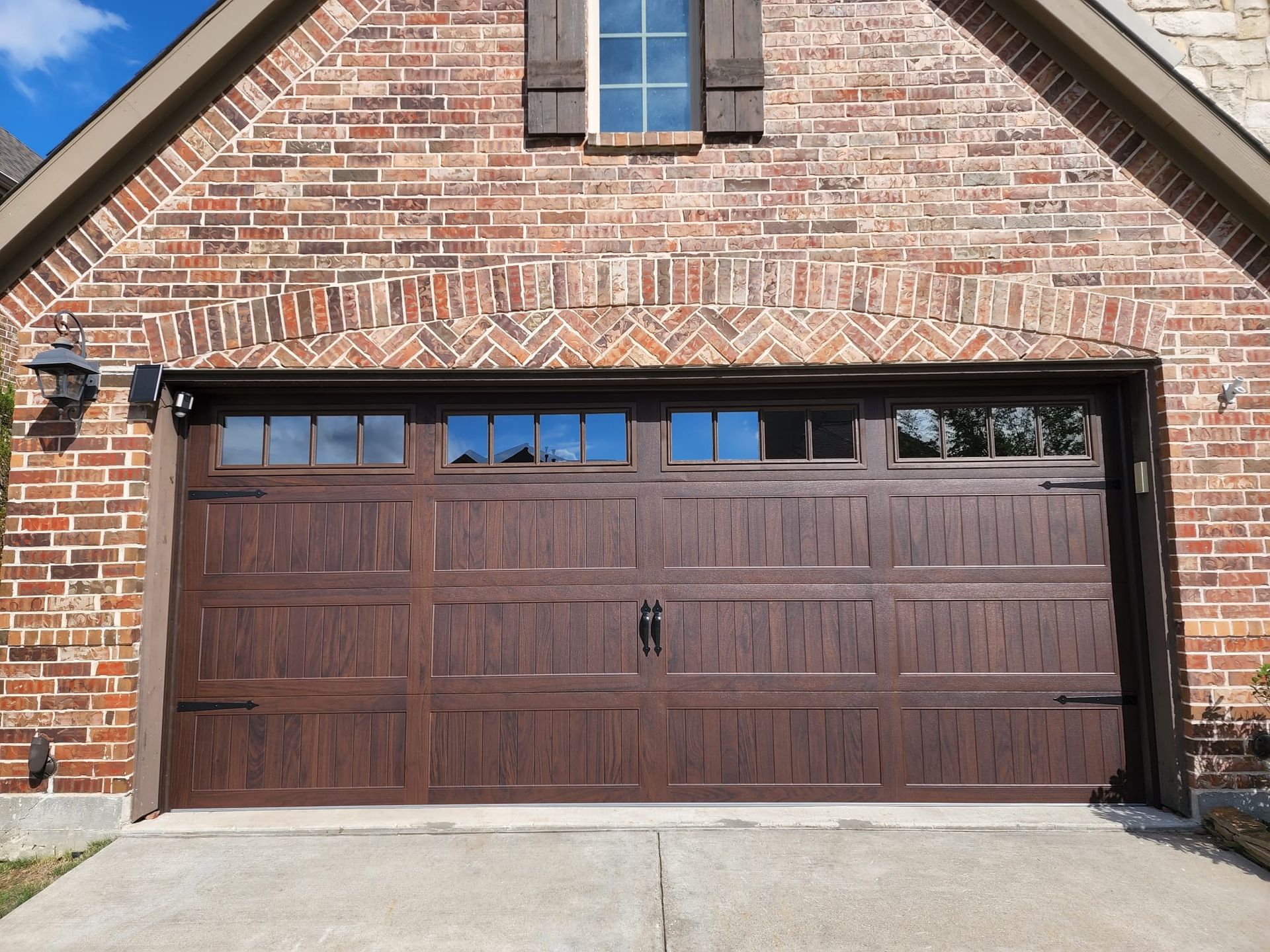 A brown garage door is sitting in front of a brick house.