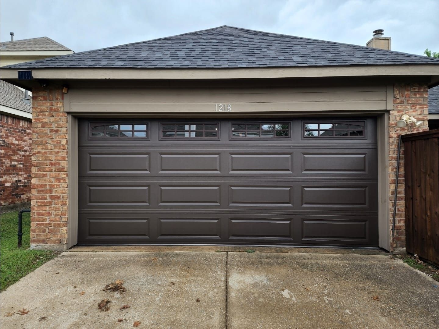A brown garage door is sitting in front of a brick house.