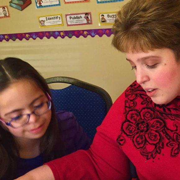 a woman in a red sweater is helping a young girl with her homework